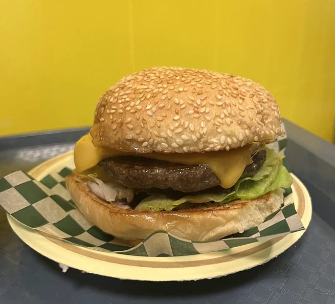 Cheeseburger with melted cheese and lettuce on a sesame bun, on green and white checkered paper