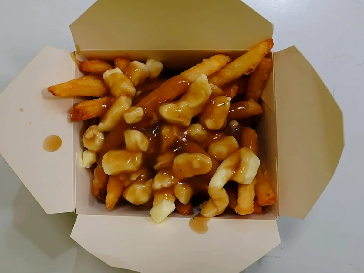 Classic poutine with fries, cheese curds and brown gravy in an open takeout box