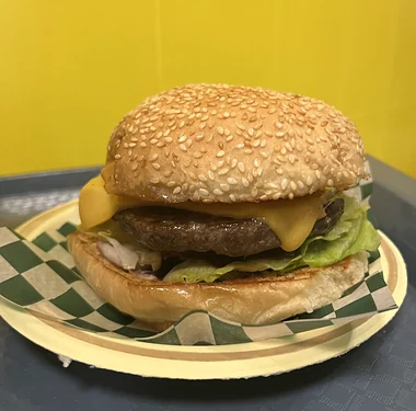 Cheeseburger with melted cheese and lettuce on a sesame bun, on green and white checkered paper