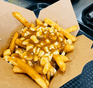 Poutine with fries, cheese curds and gravy in an open kraft takeout box, seen from above